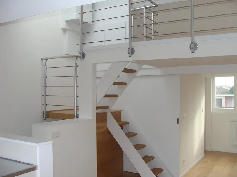 Open staircase with oak treads and a stainless steel balustrade, with a void and a mezzanine above.