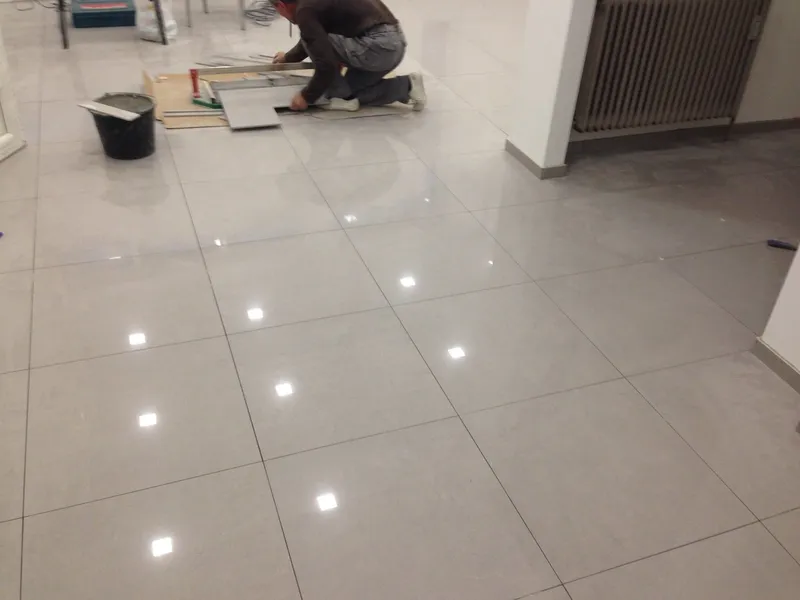 Pose de carrelage grand format ; la partie achevée du sol reflète l’éclairage du plafond.