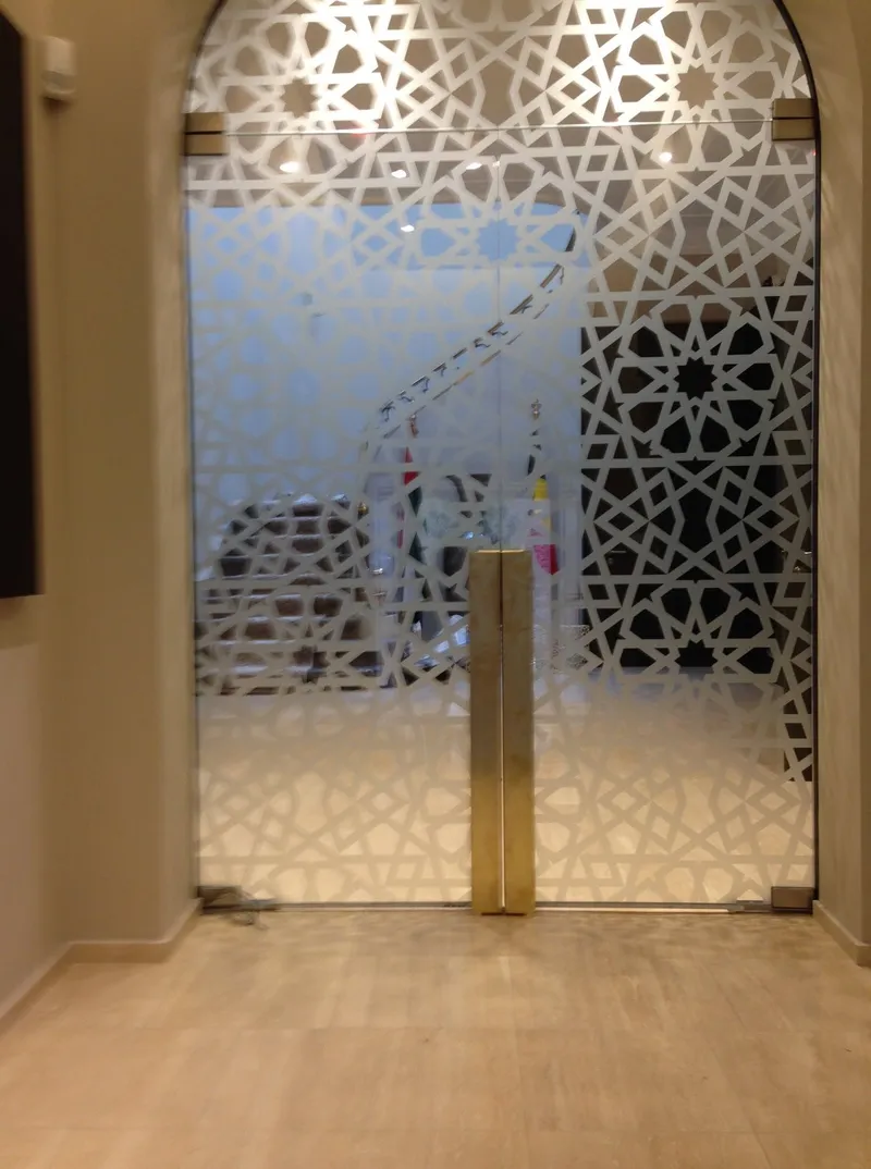 Porte vitrée à deux battants dans une baie cintrée, motif géométrique finement découpé sur le verre et poignées en laiton.