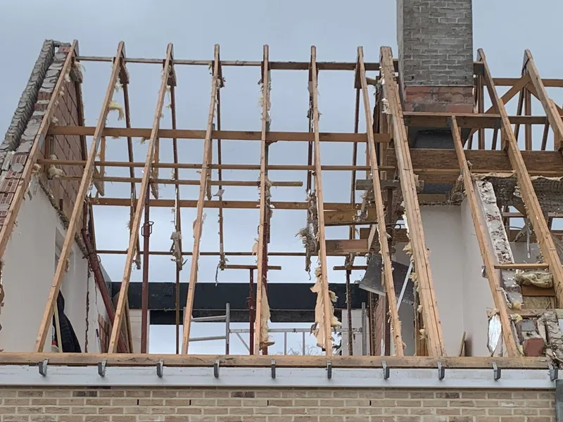 Open dakconstructie met spanten, gordingen en een gemetselde schoorsteen.
