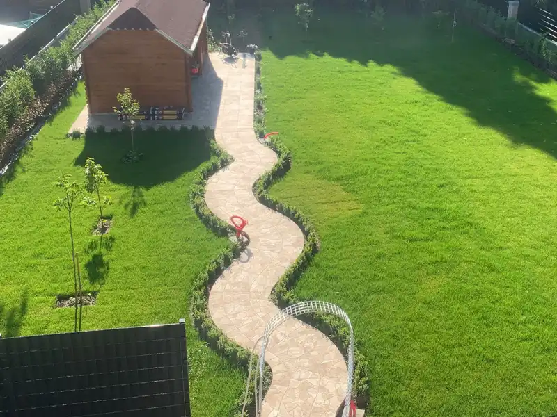 De tuin vanaf de verdieping: gazon, slingerend natuurstenen pad, hagen en een tuinhuis.