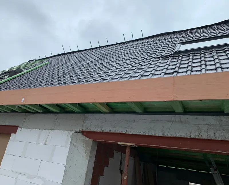 La nouvelle charpente vue d’en dessous : toiture en tuiles à moitié posée sur liteaux traités, avec fenêtre de toit, poutre lamellée-collée et linteau acier au-dessus d’un mur en béton cellulaire.