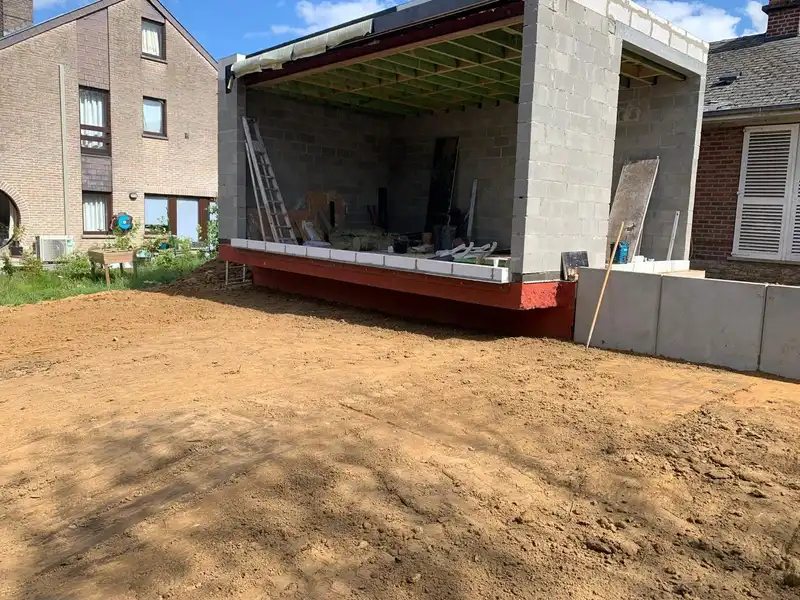 Maçonnerie en blocs et solivage en bois de l’extension, en porte-à-faux au-dessus d’une poutre de rive rouge.